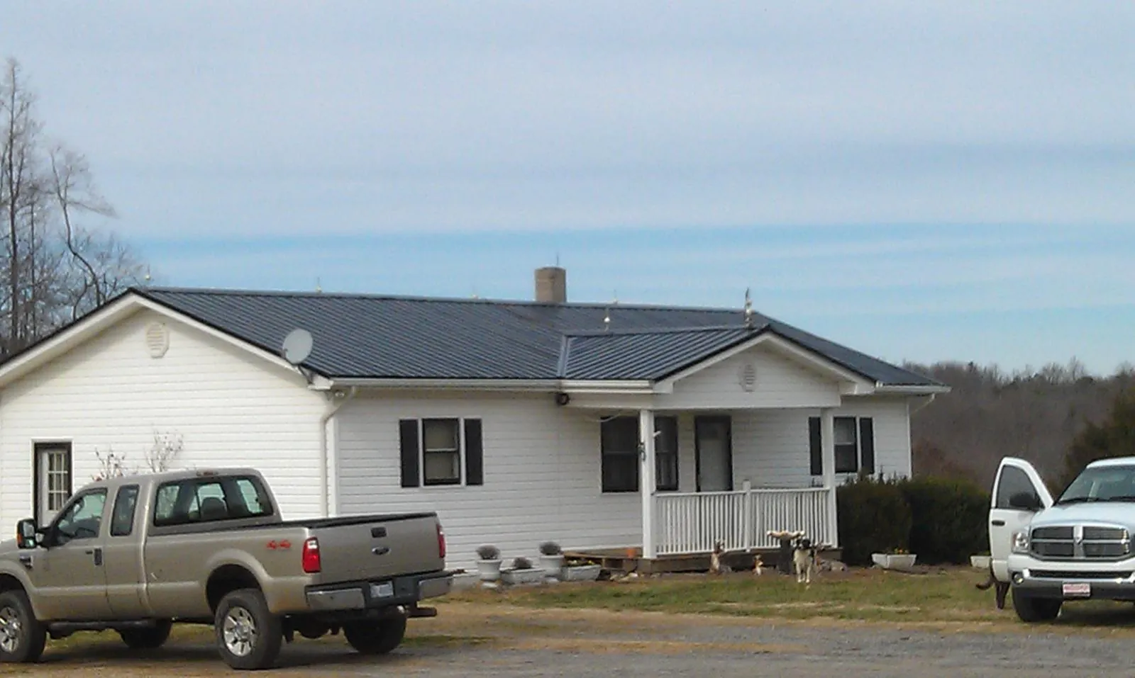 Finished dark metal roof on a white ranch home with work trucks parked in Prescott